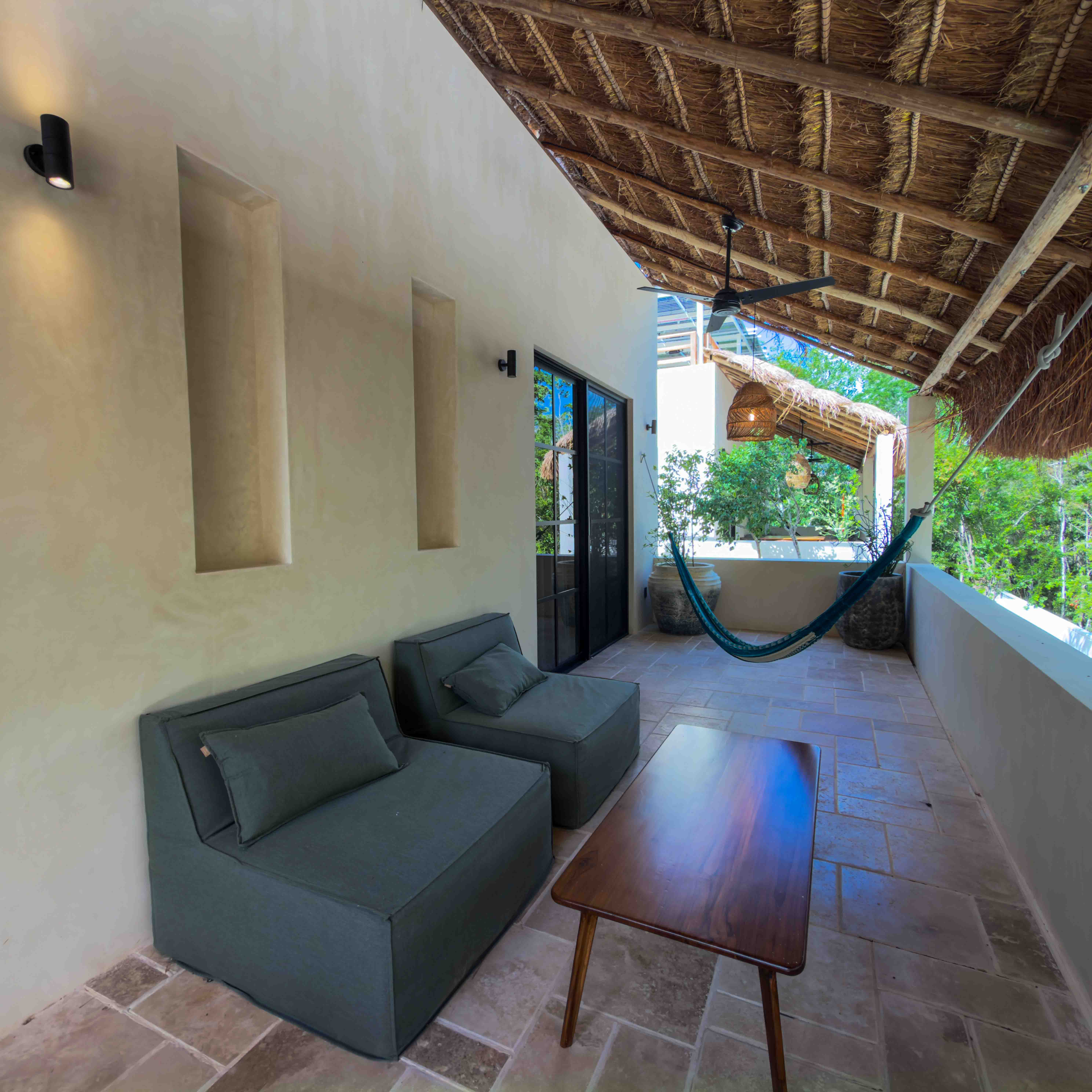 Covered balcony terrace with palapa roof, lounge chairs, coffee table, and a hammock.