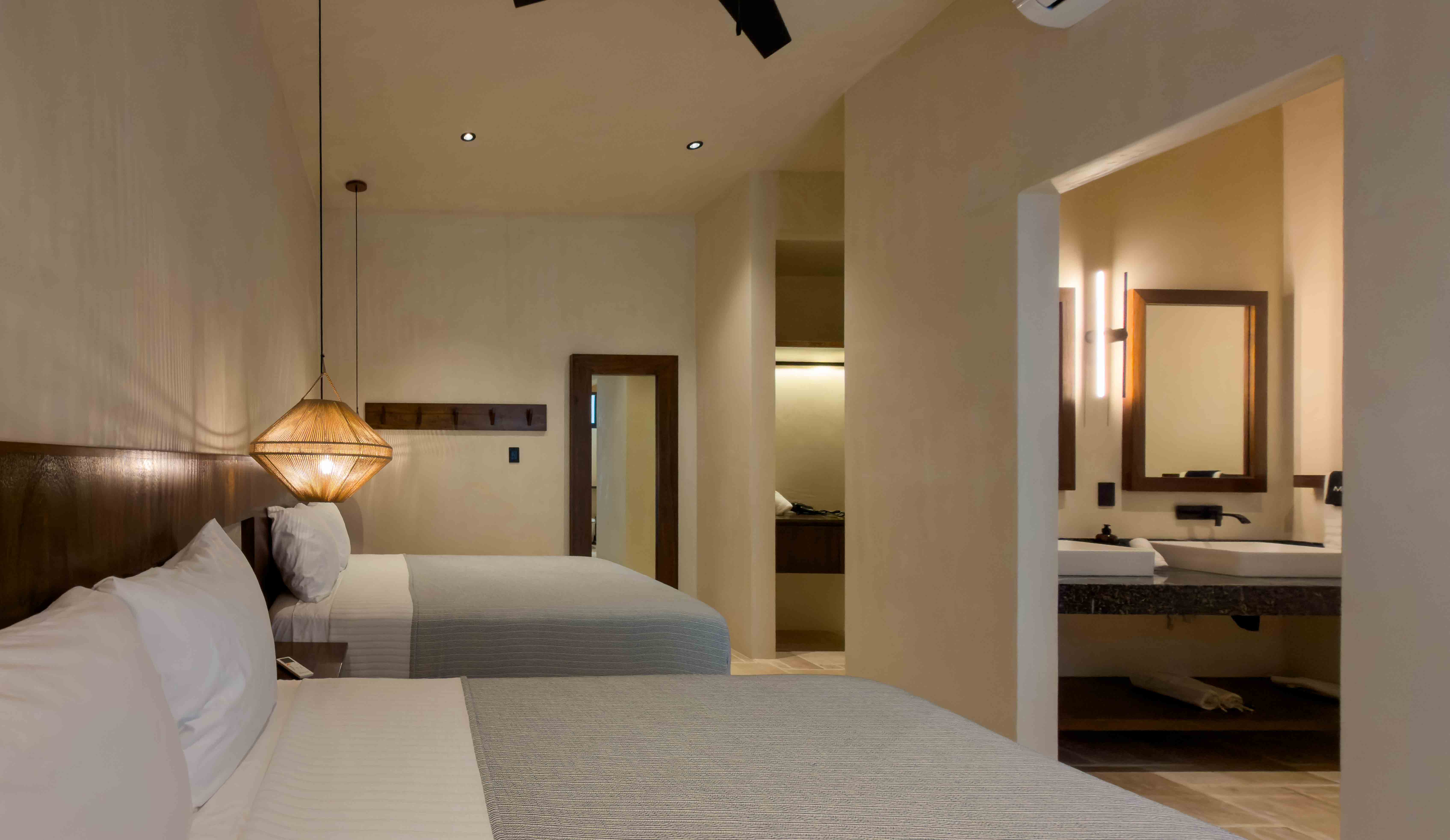 Double queen bedroom suite with warm lighting and a view into the en-suite vanity area.