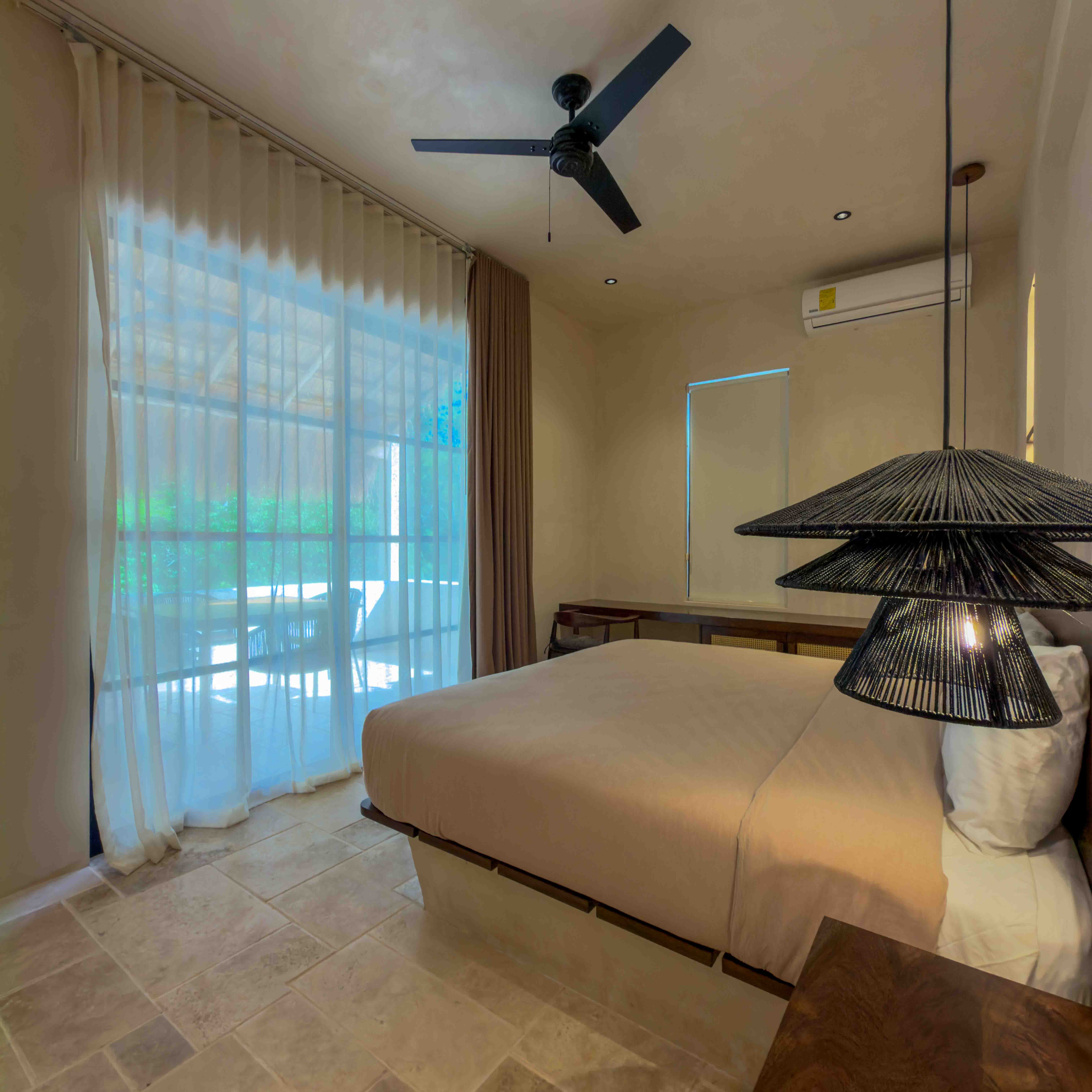 Minimalist suite with a king bed, designer woven pendant light, and floor-to-ceiling sheer curtains.