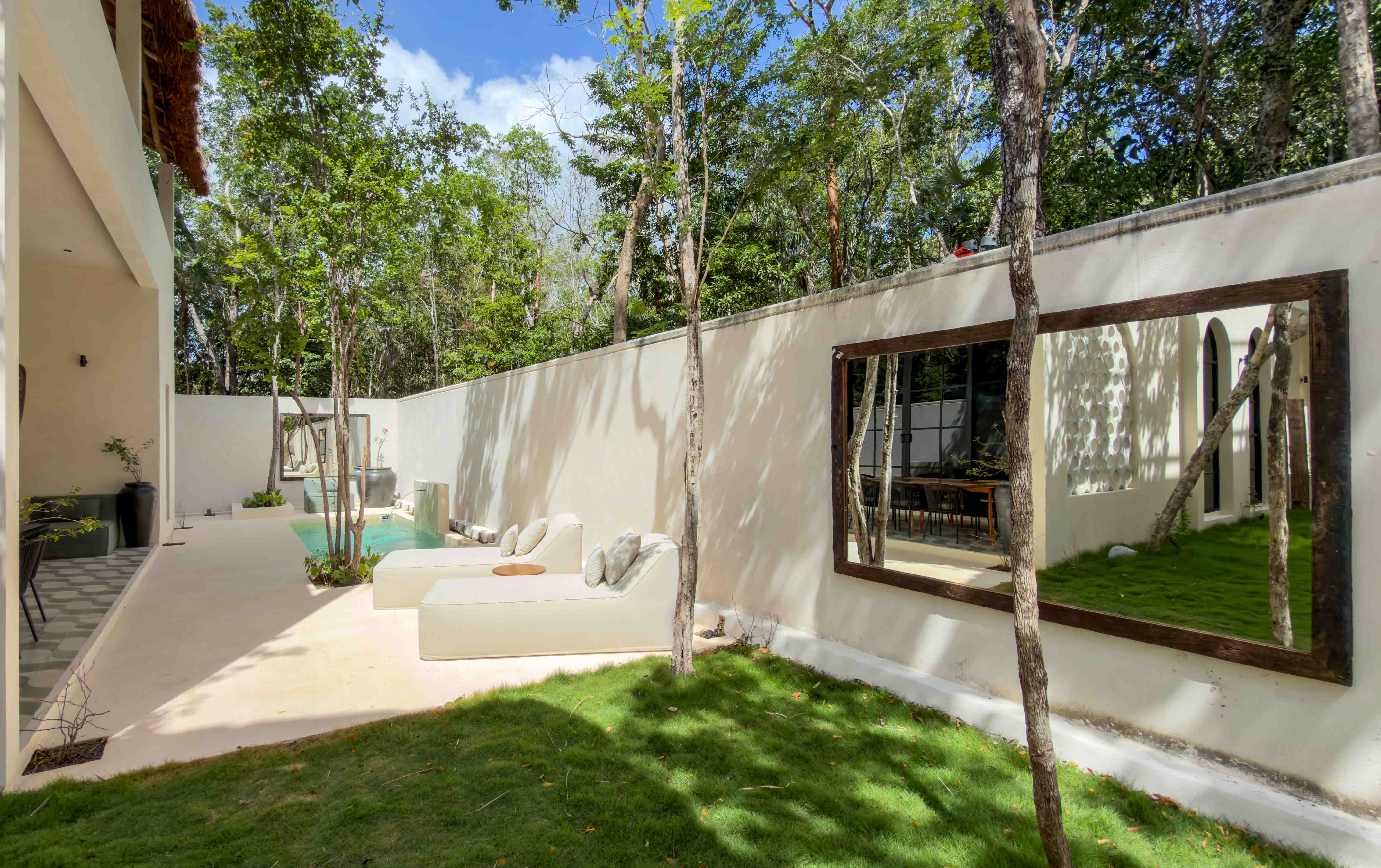 Villa courtyard featuring grass, lounge seating, and a decorative large outdoor mirror on the perimeter wall.
