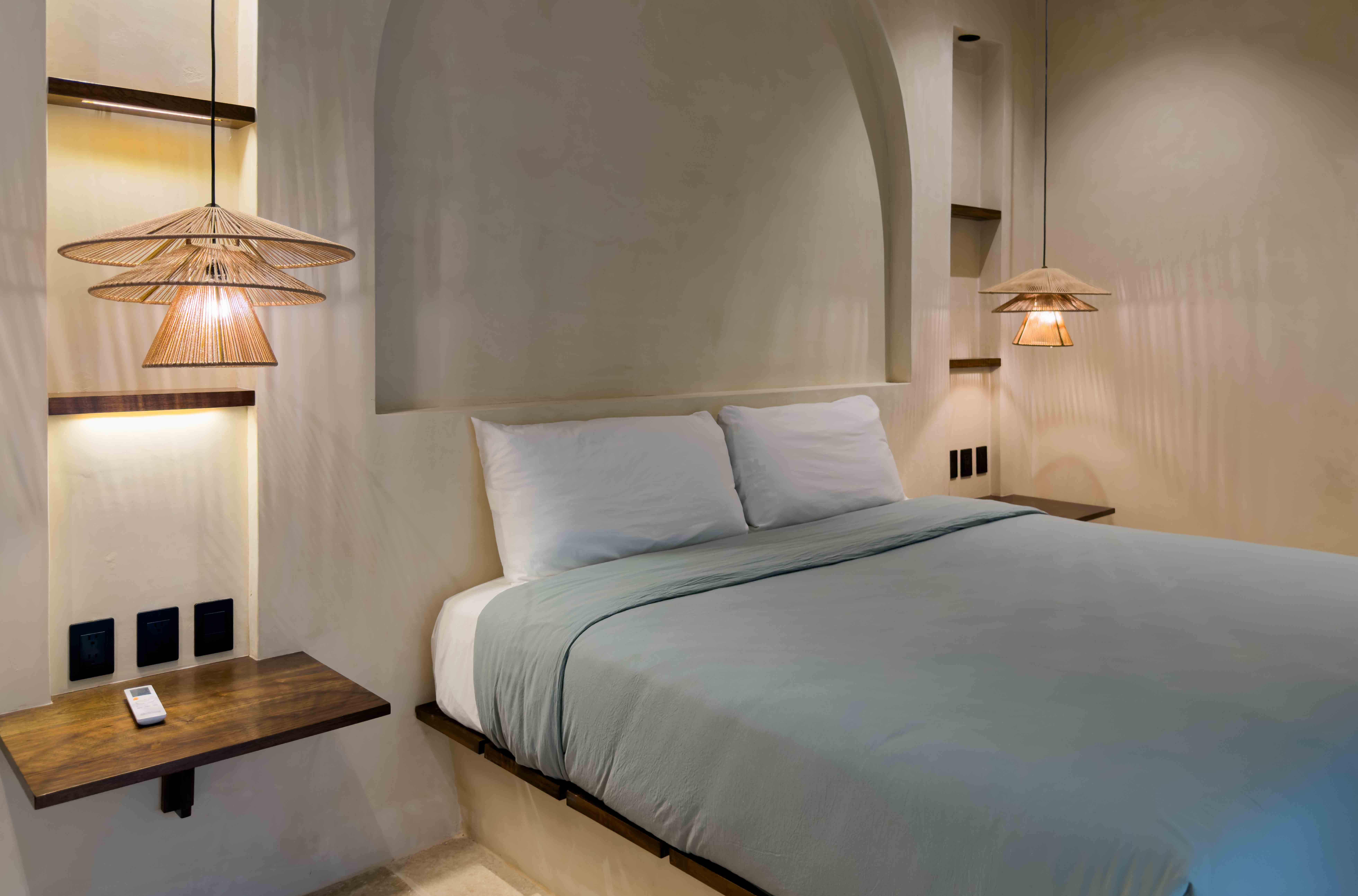 Minimalist bedroom with arched headboard detail and warm woven pendant lighting.