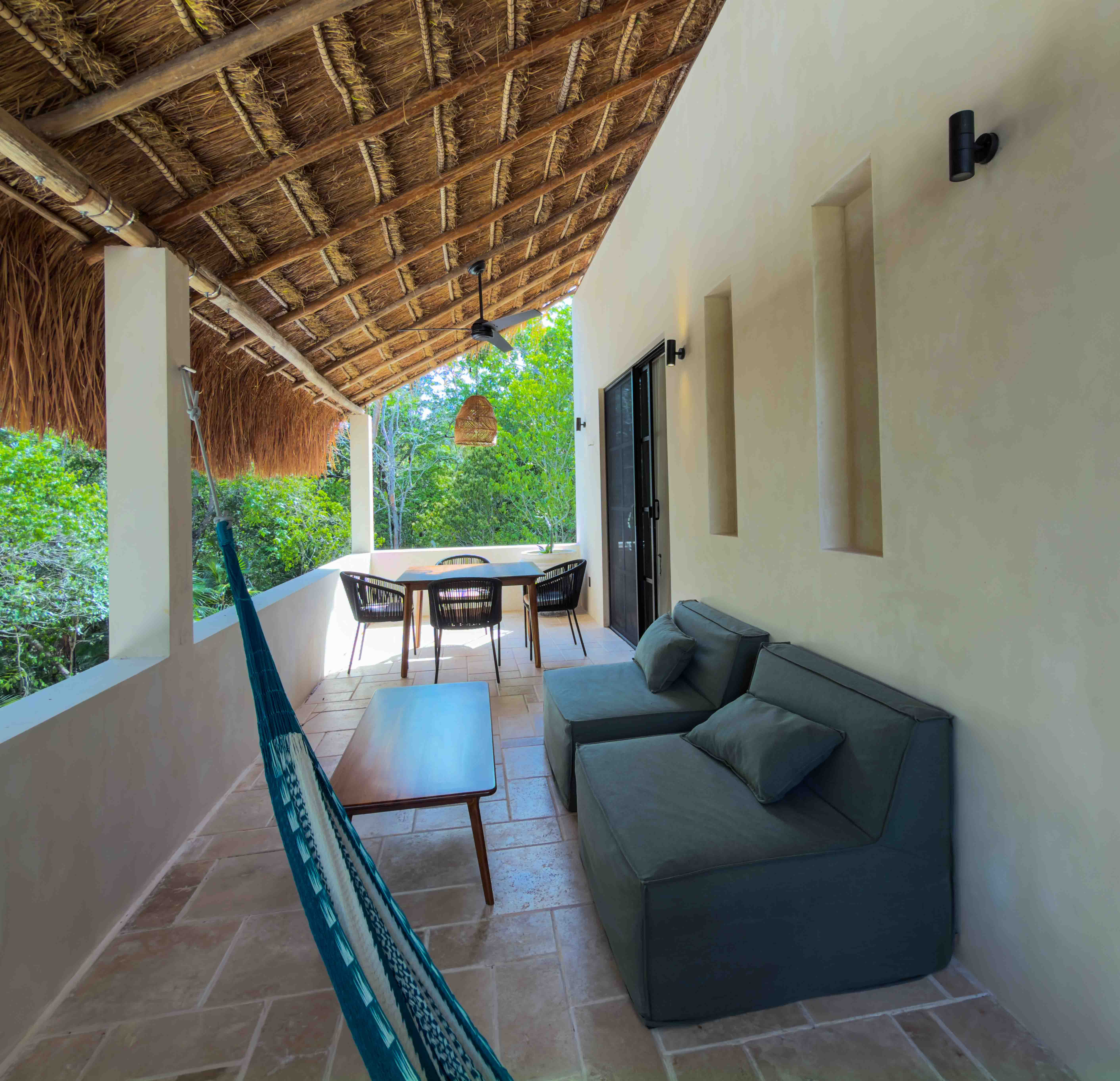Covered balcony with palapa roof, outdoor lounge seating, dining table, and a hammock.