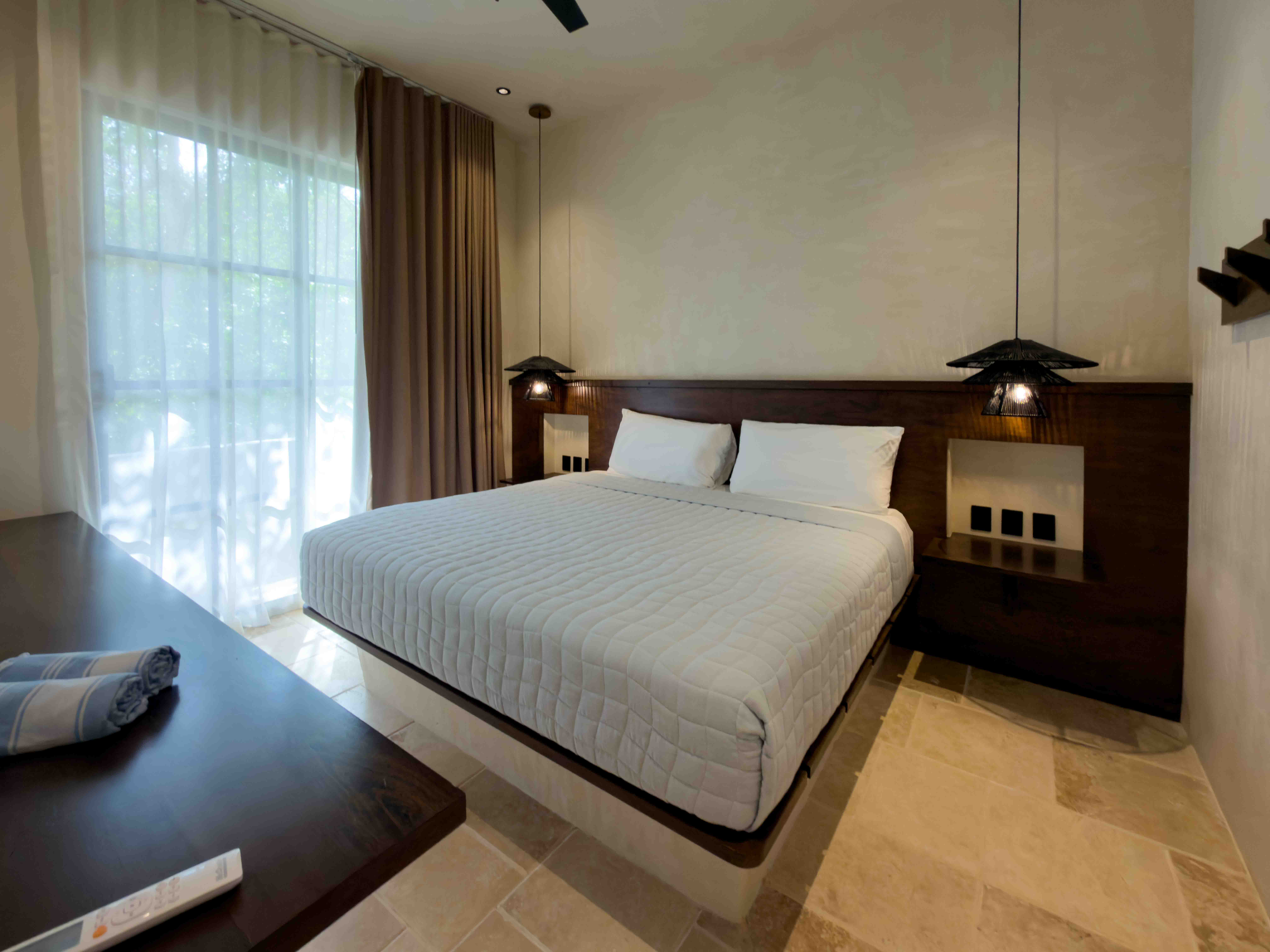 Minimalist suite with dark wood headboard, pendant lighting, and natural stone flooring.