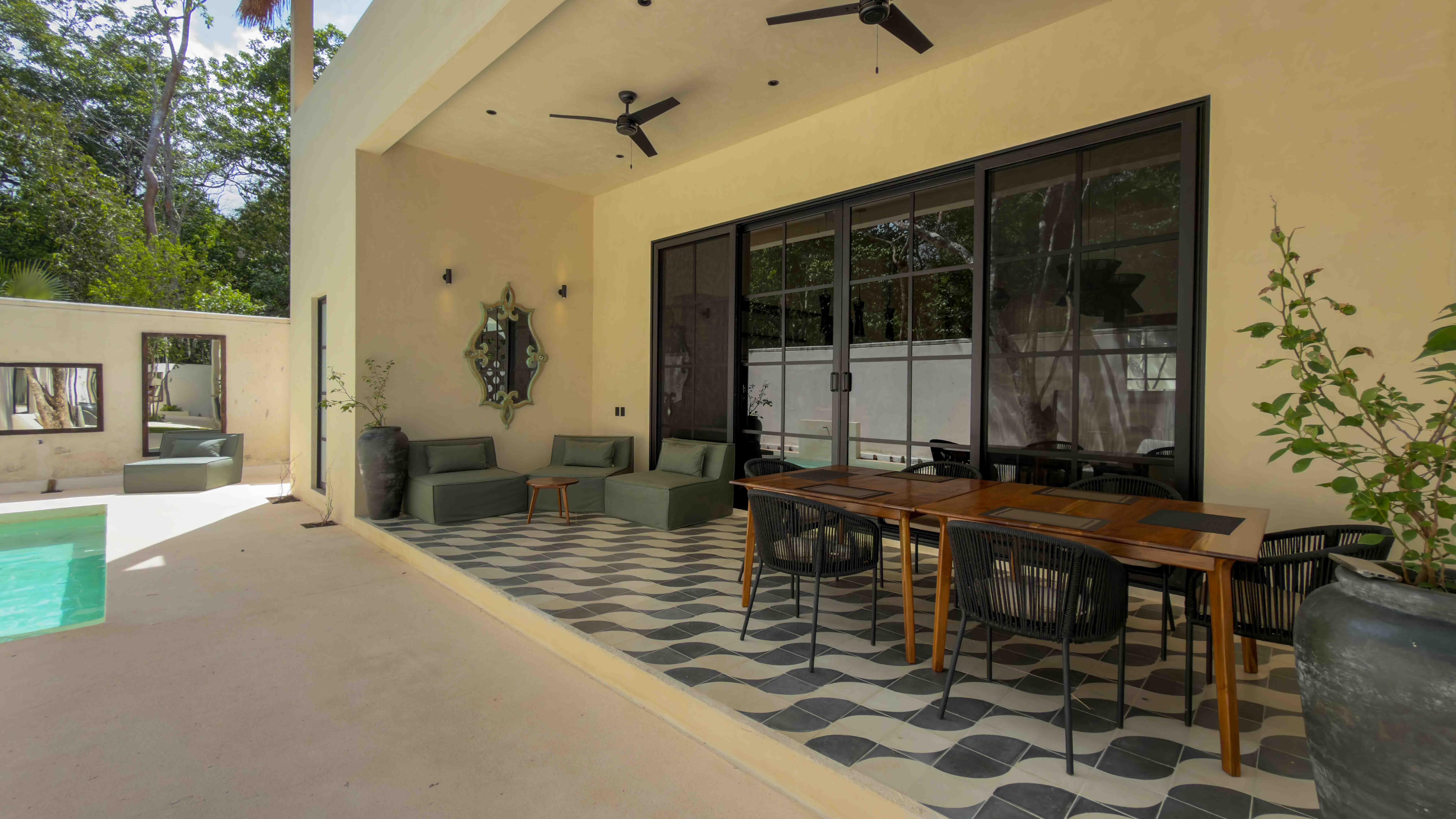Covered outdoor patio with a dining table, lounge chairs, and decorative wave tiling next to the pool area.