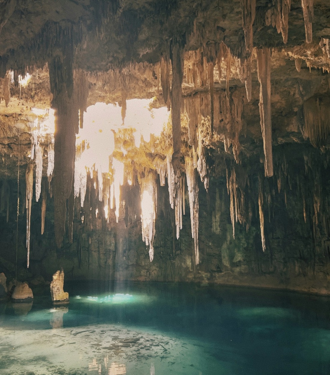Sunlight falling through stalactites into a turquoise cave cenote