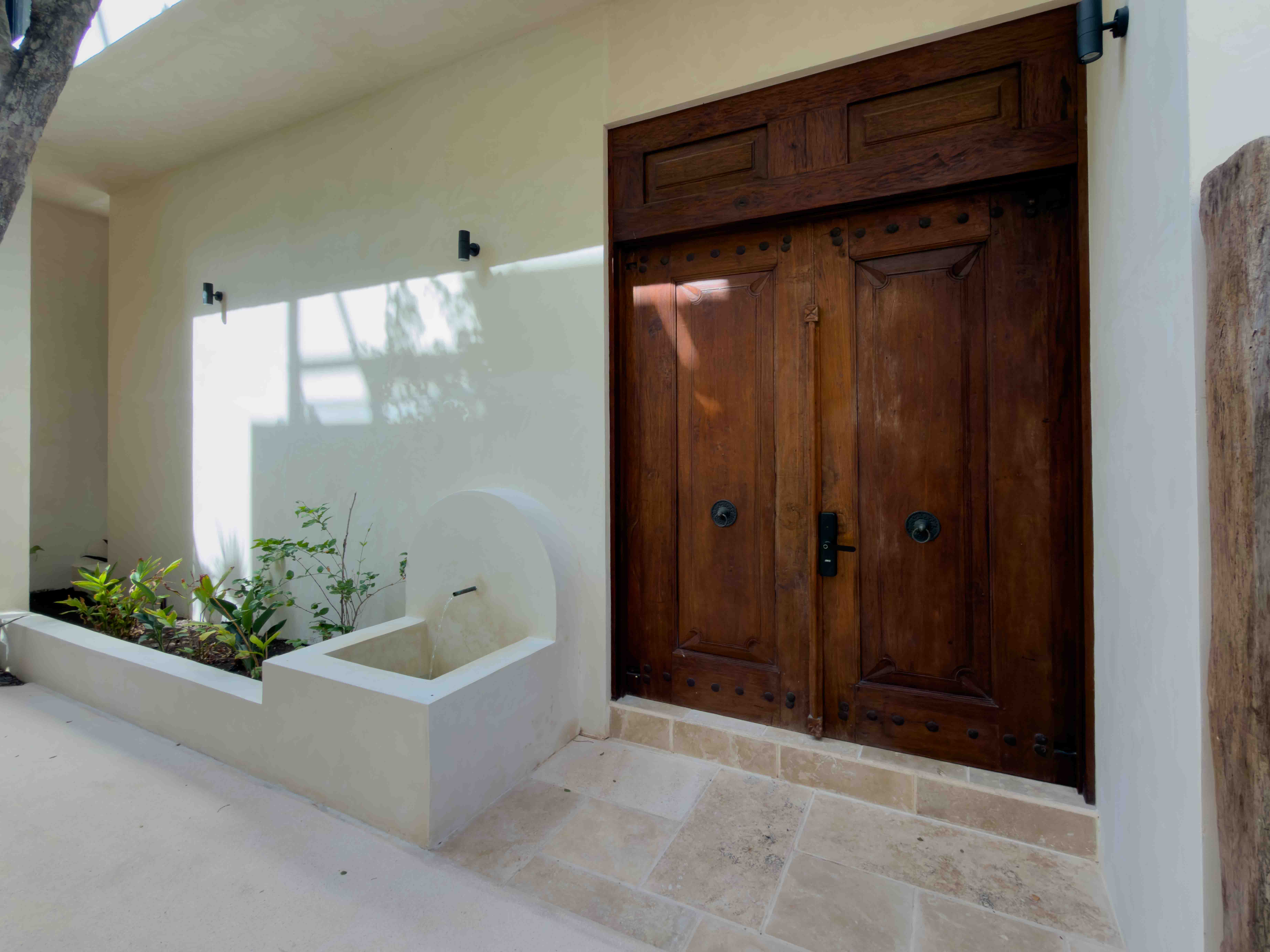 Large carved wooden entrance doors with stone courtyard and planter box.