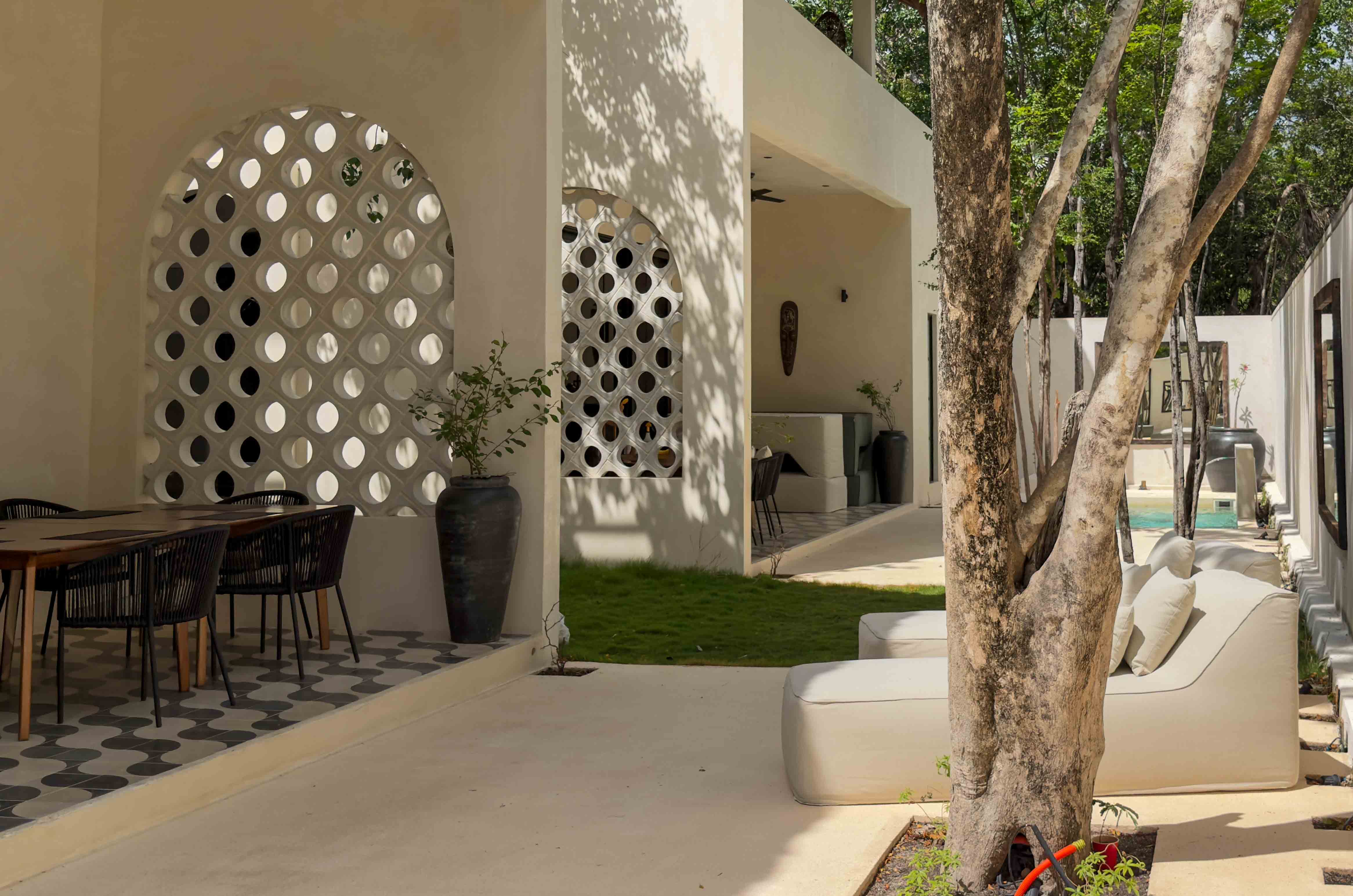 Covered outdoor dining area and patio lounge featuring geometric breeze blocks and lush landscaping.