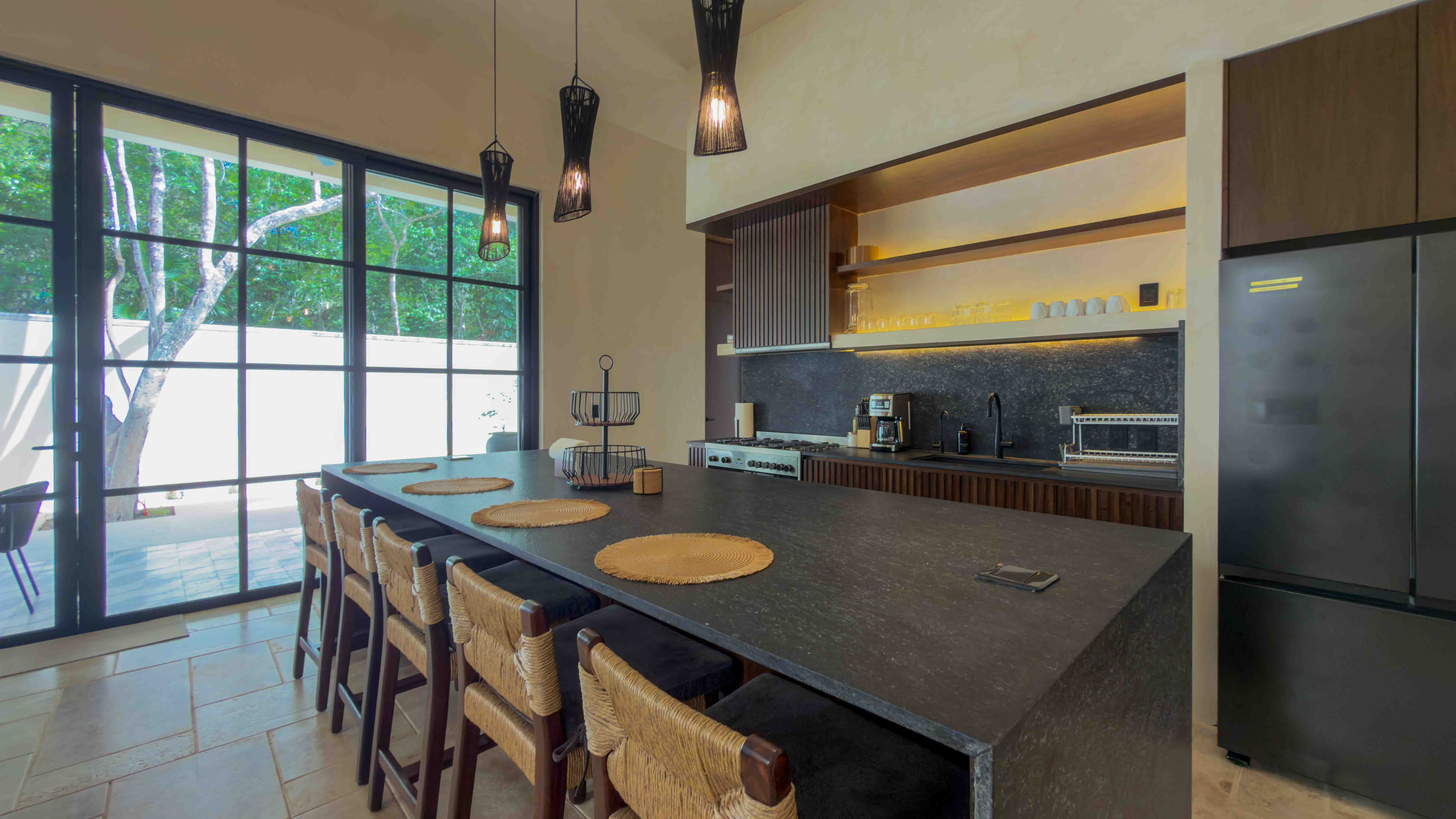Modern gourmet kitchen with large dark stone island and floor-to-ceiling windows.