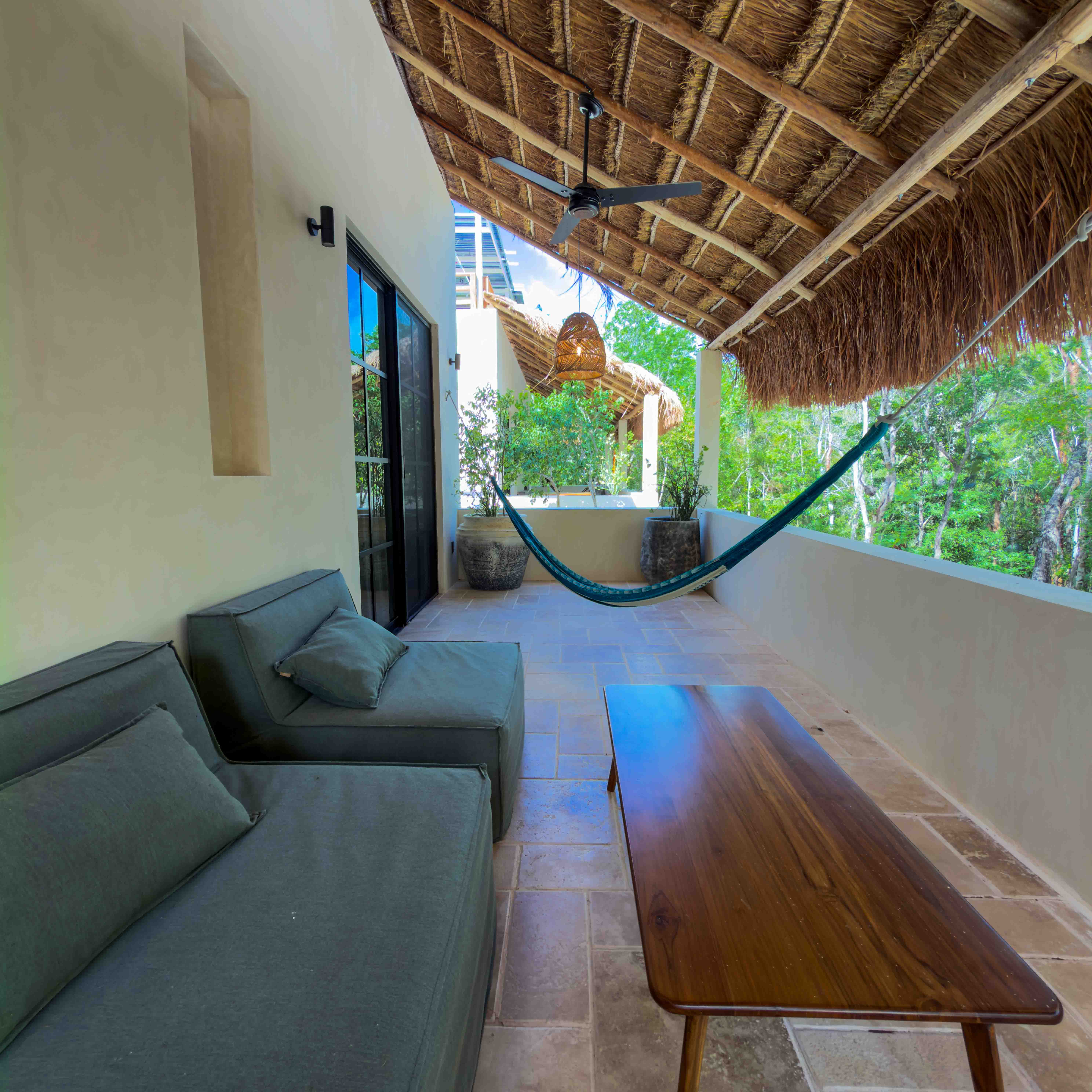 Covered balcony terrace with palapa roof, hammocks, and lounge seating overlooking jungle greenery.