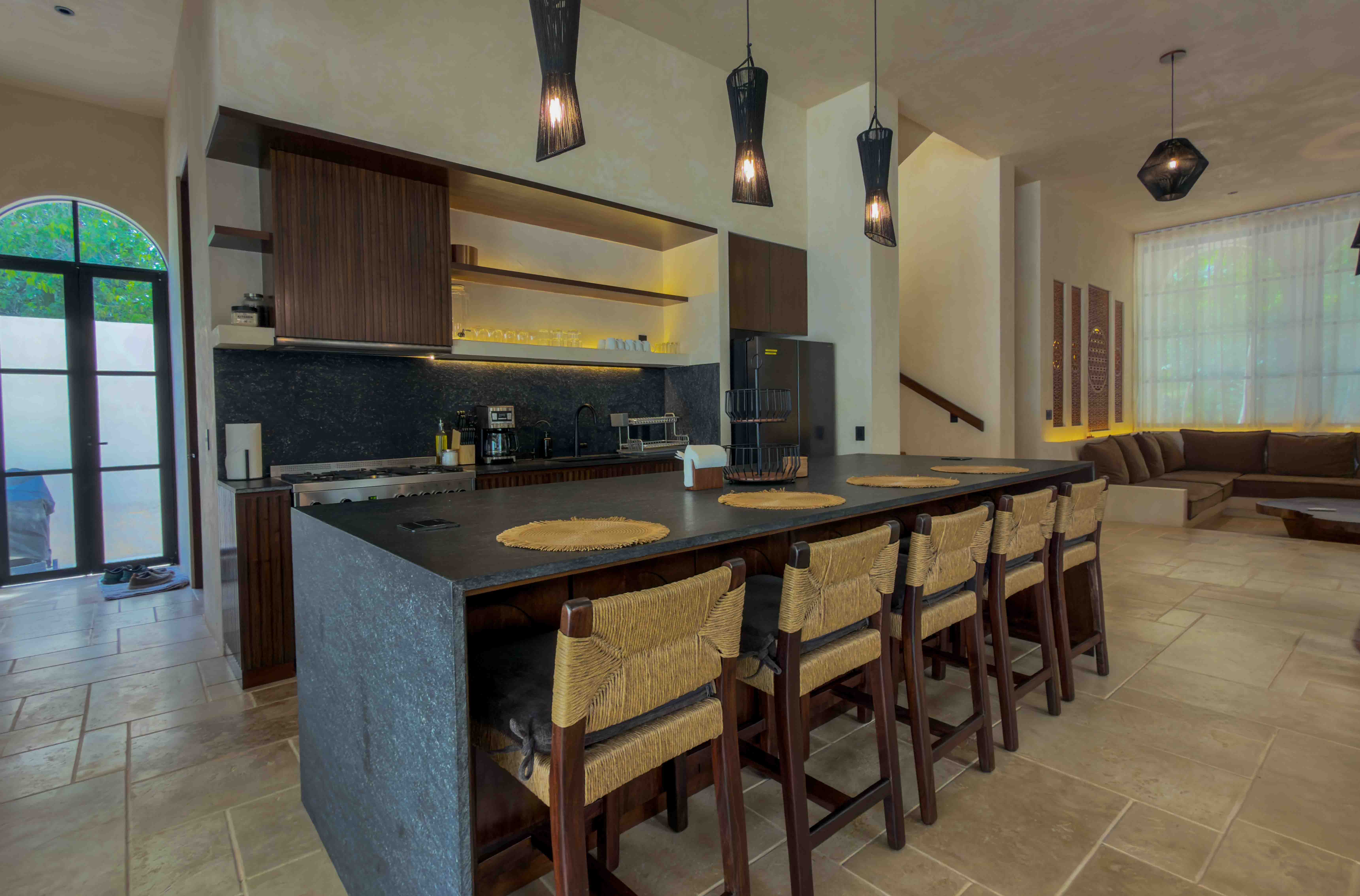 Modern kitchen with black stone island and woven bar stools in an open concept layout.