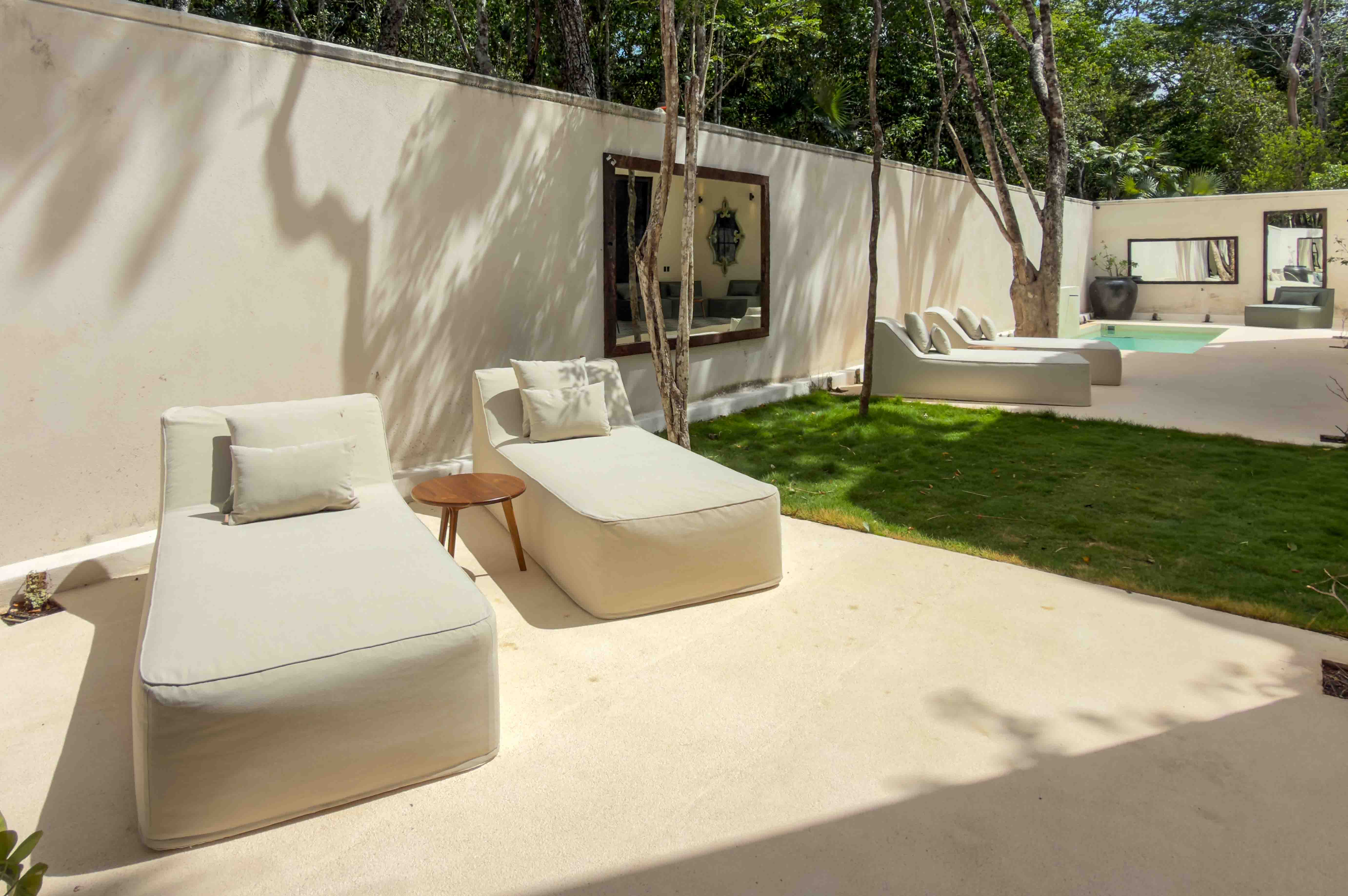 Minimalist sun loungers in a walled garden with mirrors and tropical greenery.