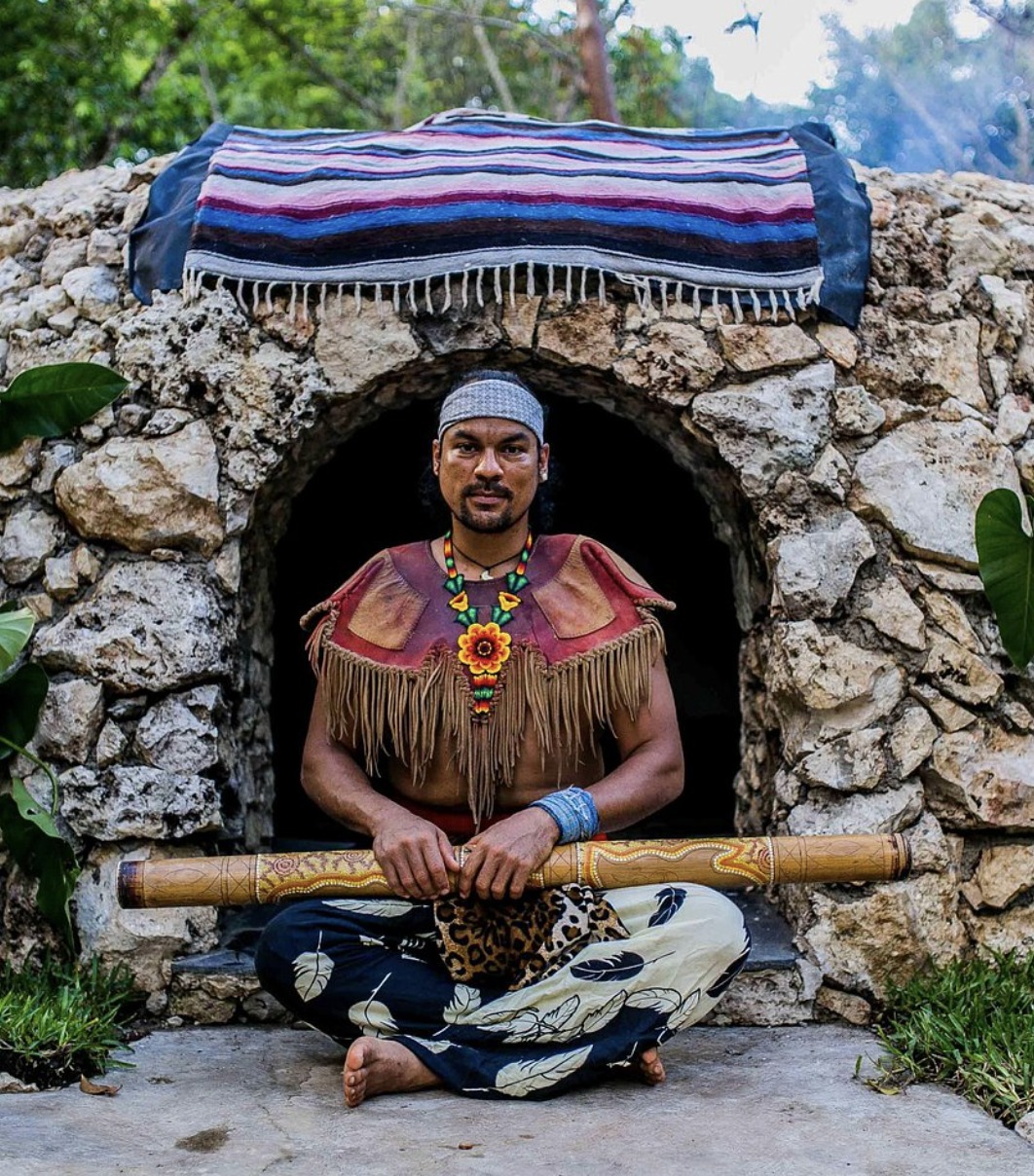 Shaman seated at the entrance of a stone temazcal sweat lodge