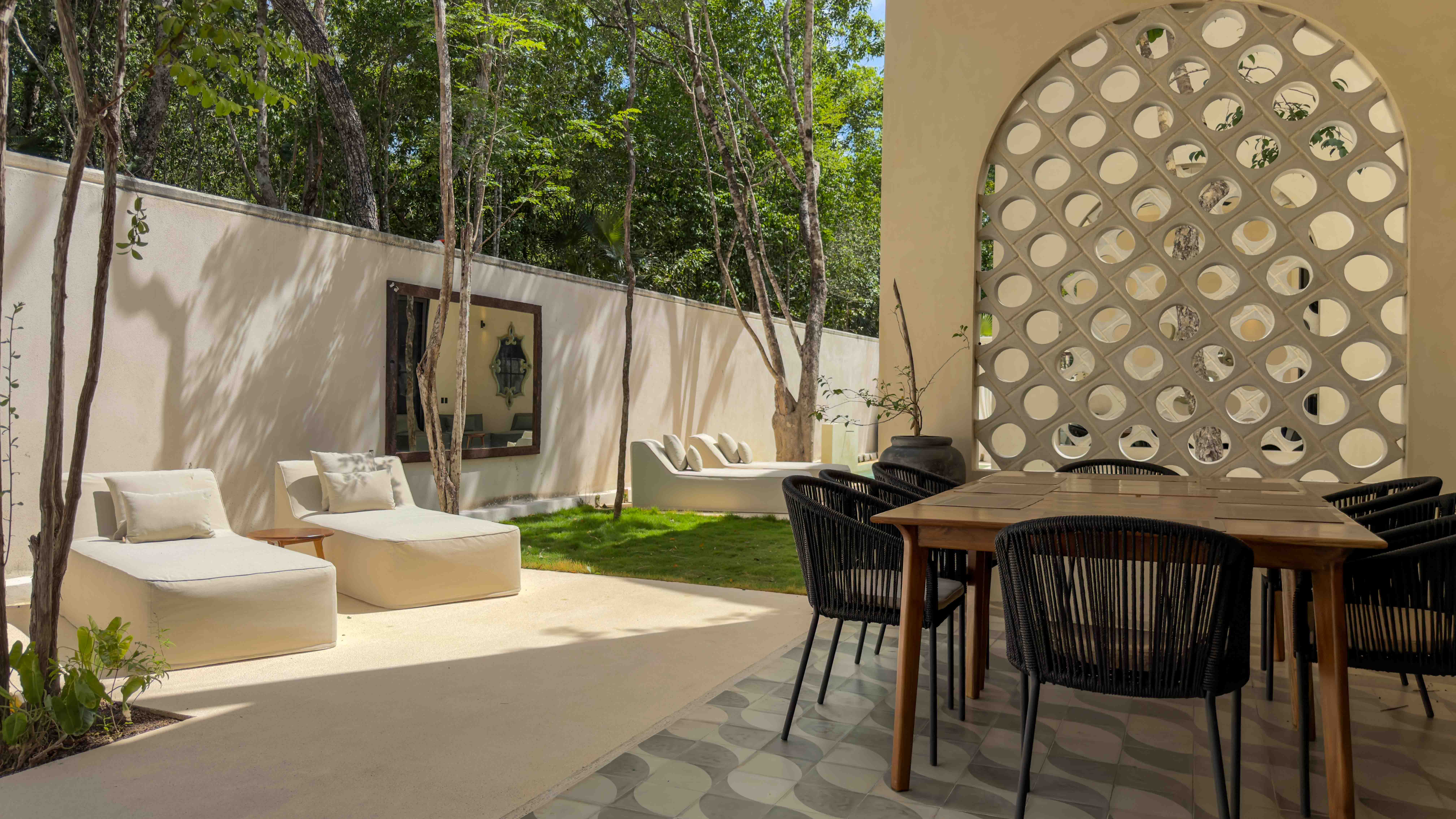 Covered outdoor dining area with modern furniture, decorative breeze blocks, and garden lounge seating.