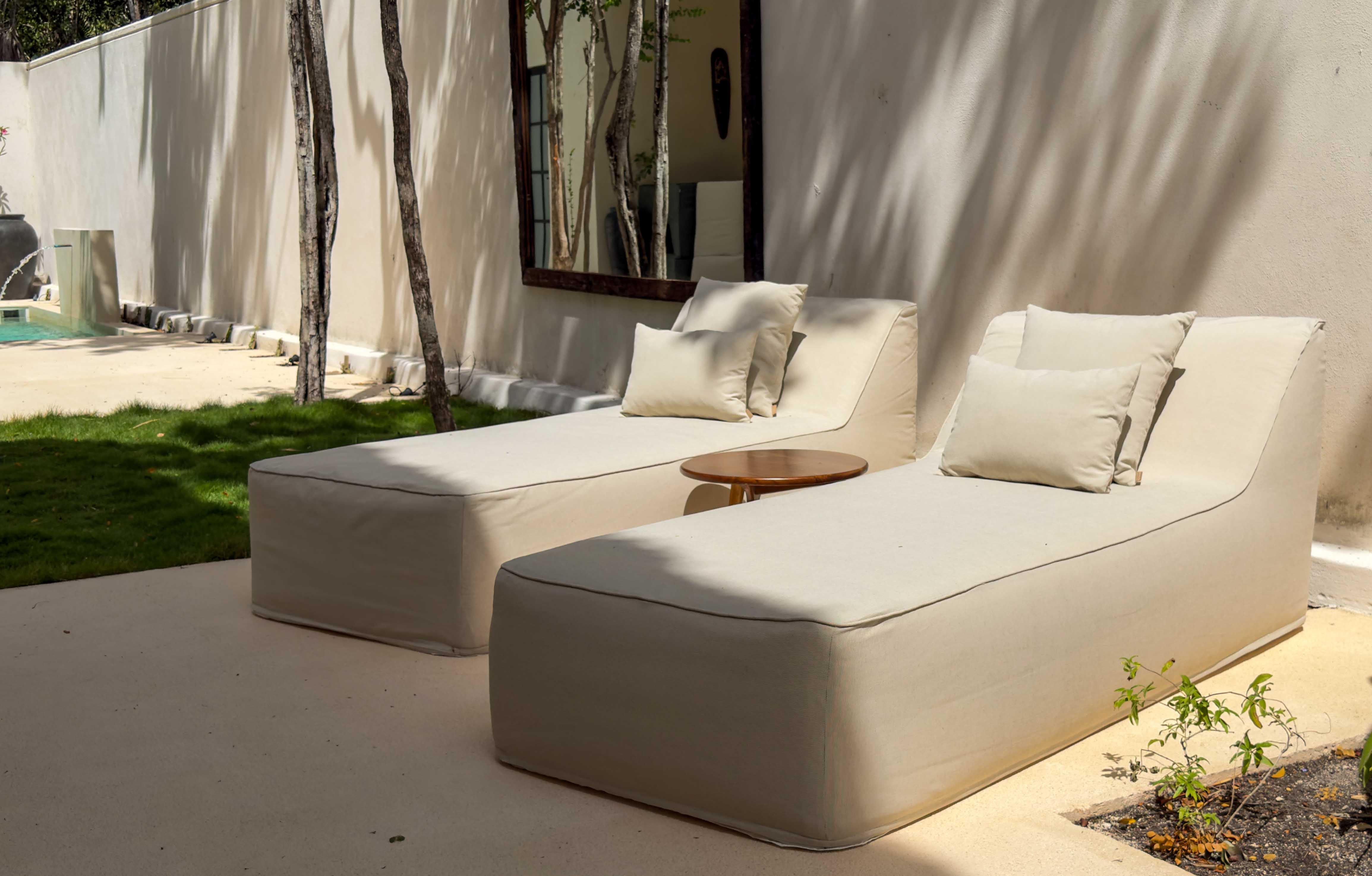 Minimalist cream lounge chairs in a sun-drenched courtyard with palm shadows.